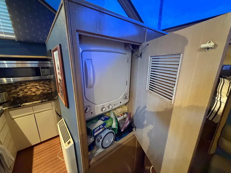 Slide: The Image of A compact washer and dryer closet in a yacht cabin with a kitchen area in the background. - 42