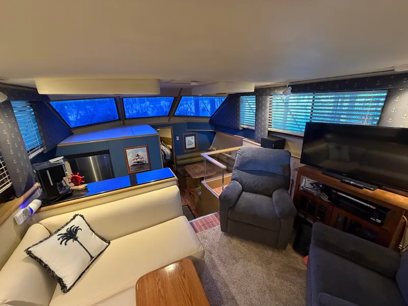 Slide: The Image of The interior of a 1991 Hatteras 52 Cockpit Motor Yacht features a cozy seating area with a sofa, armchair, TV, and large windows. - 33