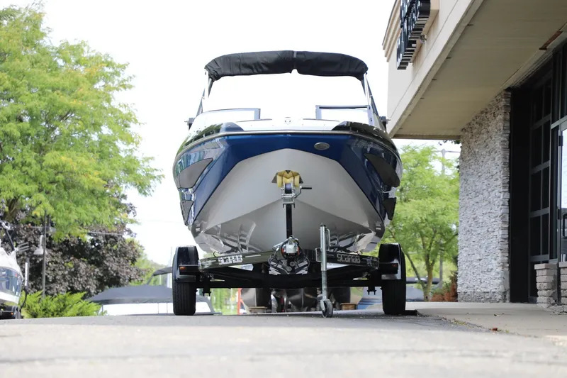 Slide: The Image of 2023 Scarab 195 ID boat on trailer, parked near building, surrounded by trees. - 2