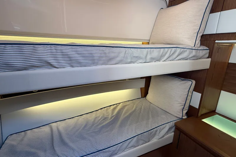 Slide: The Image of Bunk beds in the 2026 Tiara Yachts EX 54 cabin, featuring striped bedding and wood accents. - 22
