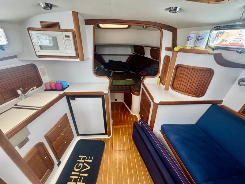 Slide: The Image of Interior of a 2003 Legacy 34 Express with wood flooring, blue seating, and a compact kitchen. - 25