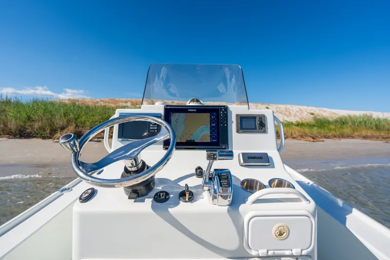 Slide: The Image of 2013 Yellowfin 24 Bay boat dashboard with navigation system, steering wheel, and controls near sandy shore. - 14