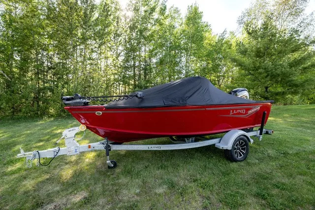 Slide: The Image of A red 2027 Lund 1700 Adventure Sport boat on a trailer, surrounded by trees. - 2