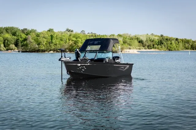 The Image of A 2027 Lund 1700 Adventure Sport boat floats on a calm lake with a wooded shoreline. - 1