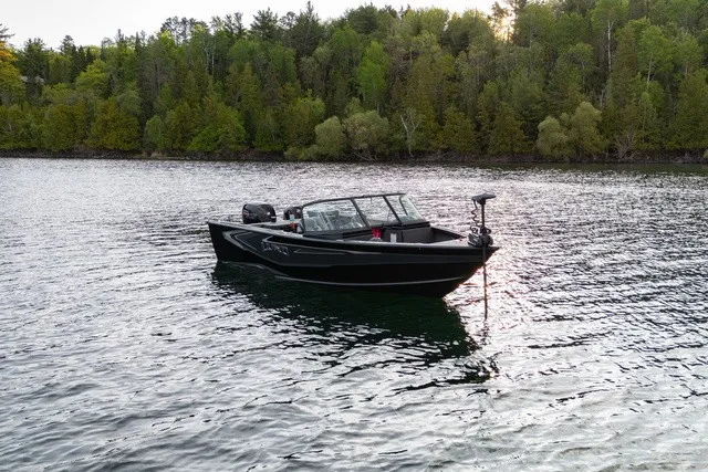 Slide: The Image of A black boat floating on a calm lake, surrounded by wooded shores. - 7