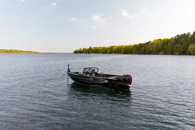Slide: The Image of A 2027 Lund 1875 Fisherman boat floats on a calm lake, surrounded by trees. - 8