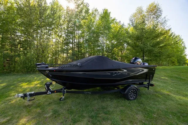 Slide: The Image of A 2027 Lund 1875 Fisherman boat on a trailer, set on a grassy area with trees behind. - 6