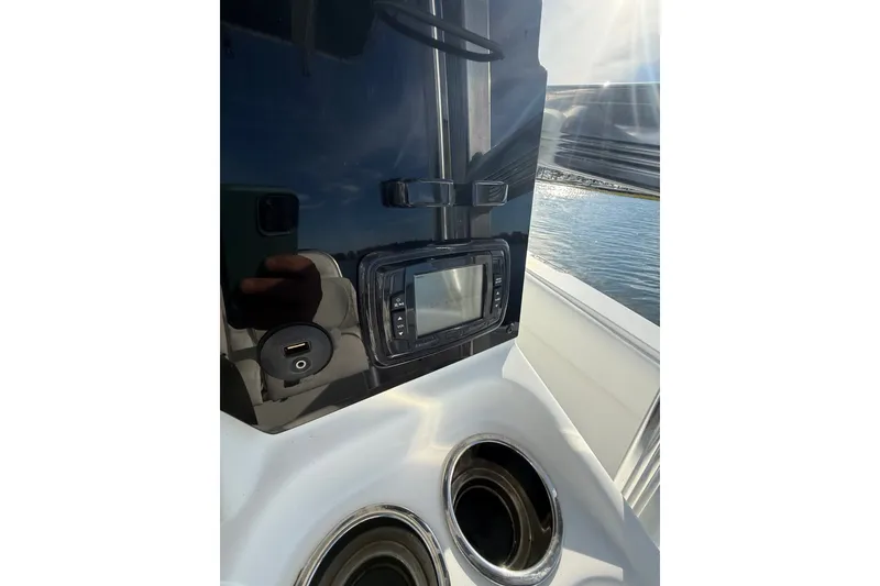 Slide: The Image of 2018 Sea Hunt Ultra 211 boat dashboard with controls and cup holders, near water. - 14