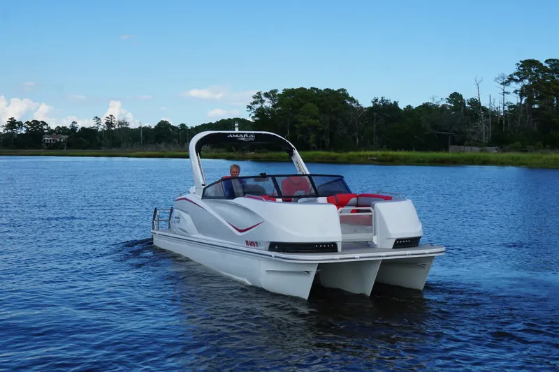 Slide: The Image of 2021 Amara pontoon boat cruising on a serene lake with lush greenery. - 2