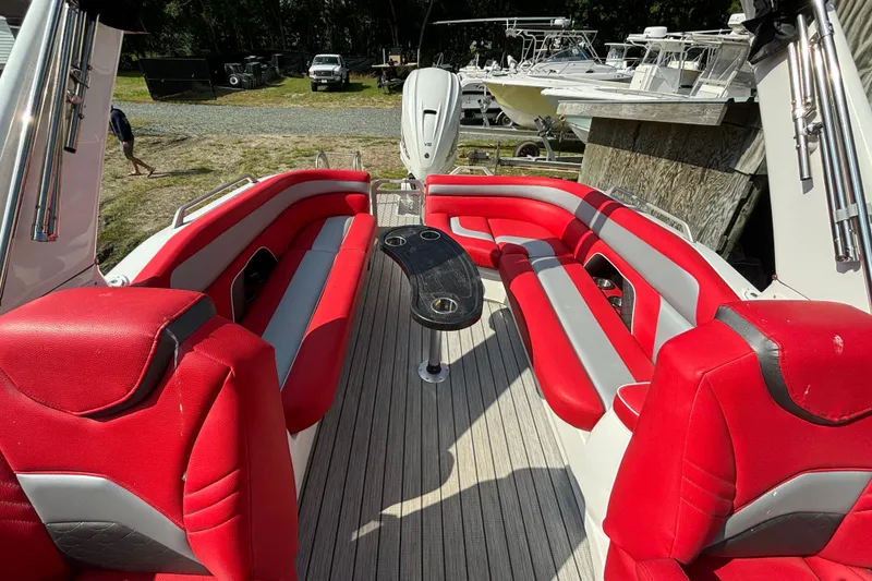 Slide: The Image of 2021 Amara pontoon boat interior with red and gray seating, docked near other boats. - 13