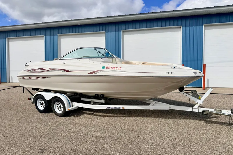 Slide: The Image of 2000 Sea Ray 210 Sundeck boat on trailer, parked outside blue storage units. - 0