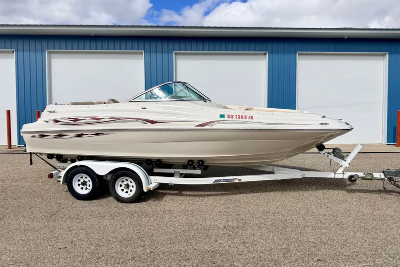 Slide: The Image of 2000 Sea Ray 210 Sundeck boat on trailer, parked outside blue garage. - 2