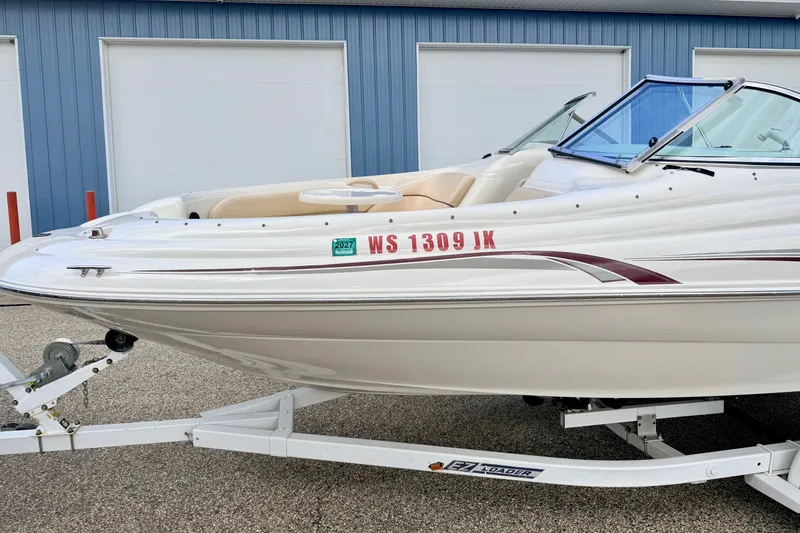 Slide: The Image of 2000 Sea Ray 210 Sundeck boat on trailer, parked near blue building. - 6