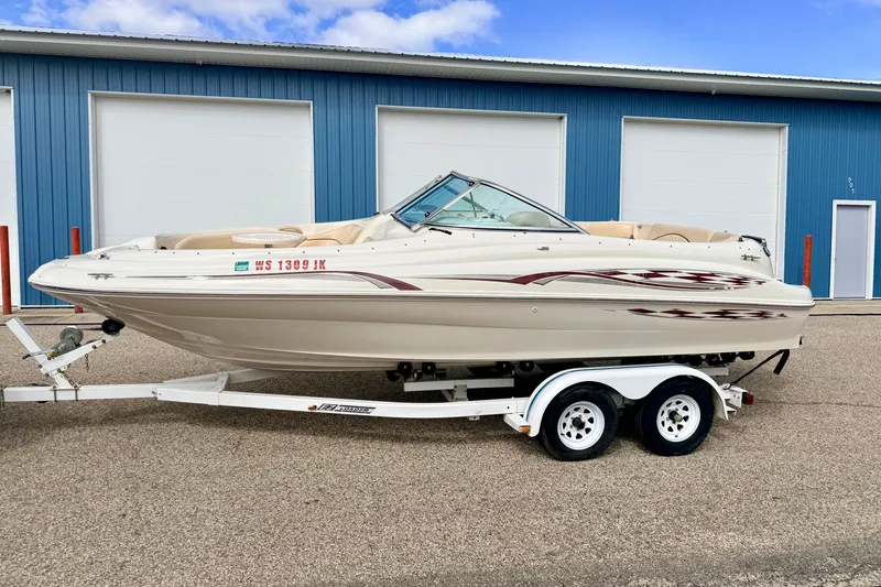Slide: The Image of 2000 Sea Ray 210 Sundeck boat on trailer, parked outside blue building. - 1