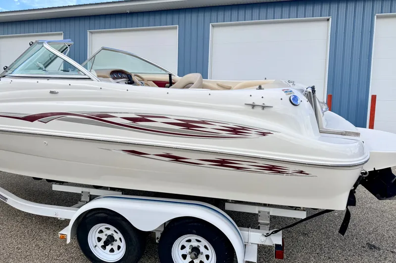 Slide: The Image of 2000 Sea Ray 210 Sundeck boat on trailer, parked near blue building. - 7