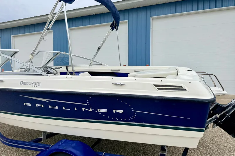 Slide: The Image of 2007 Bayliner 195 Discovery boat with blue and white exterior, parked near a blue building. - 7