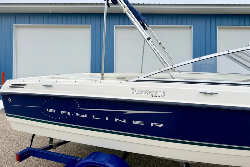 Slide: The Image of 2007 Bayliner 195 Discovery boat with blue and white exterior, parked near a blue building. - 12