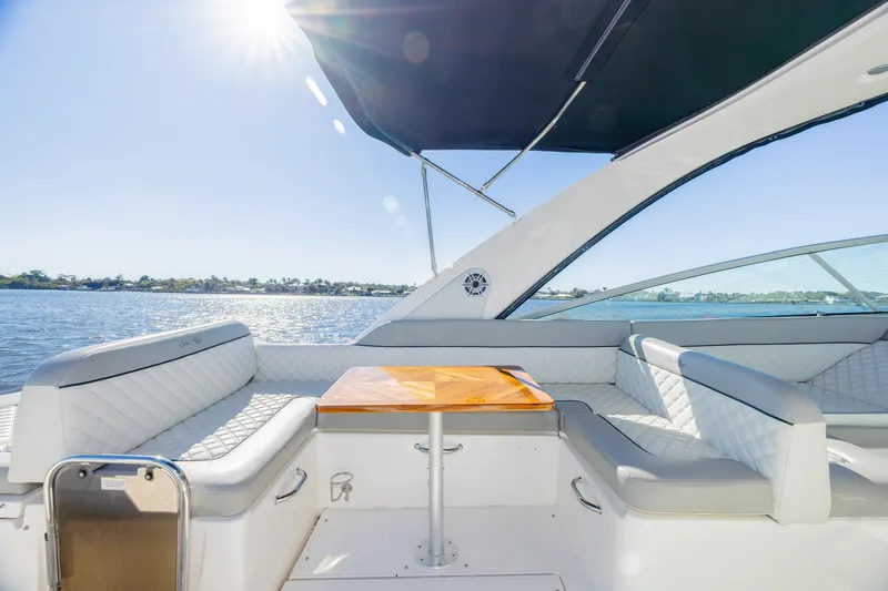 Slide: The Image of 2013 Sea Ray 370 Venture boat interior with sunlit seating and table on a calm water backdrop. - 29