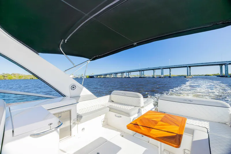 Slide: The Image of 2013 Sea Ray 370 Venture boat interior with seating, table, and water view under a bridge. - 2