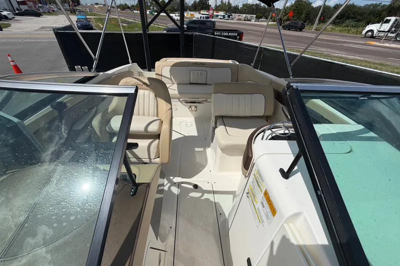 Slide: The Image of 2014 Sea Ray 240 Sundeck interior with beige seating and windshield, parked outdoors. - 66
