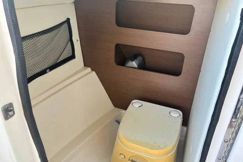 Slide: The Image of 2014 Sea Ray 240 Sundeck interior with portable toilet and storage shelves. - 33