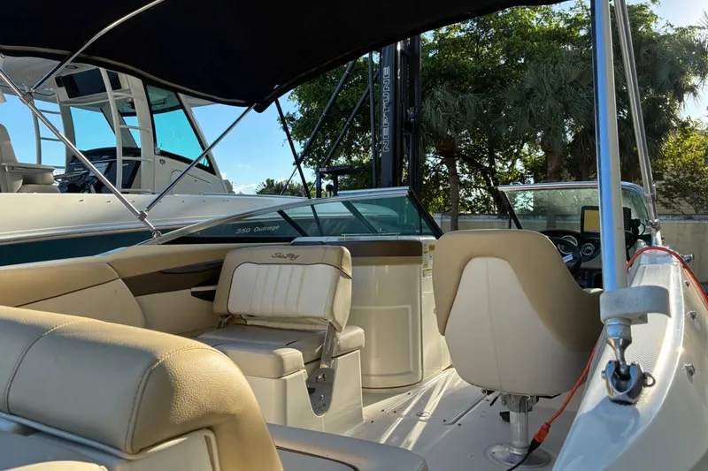 Slide: The Image of 2014 Sea Ray 240 Sundeck interior with beige seating and canopy, docked near trees. - 27
