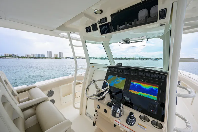 Slide: The Image of 2018 Boston Whaler 380 Outrage helm with navigation screens, steering wheel, and waterfront view. - 14