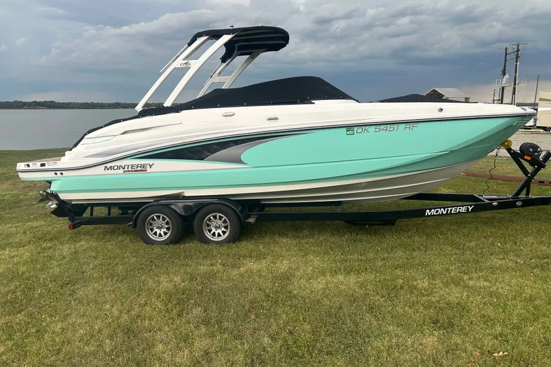 Slide: The Image of 2023 Monterey M6 boat on trailer, parked on grass by a lake under cloudy sky. - 0