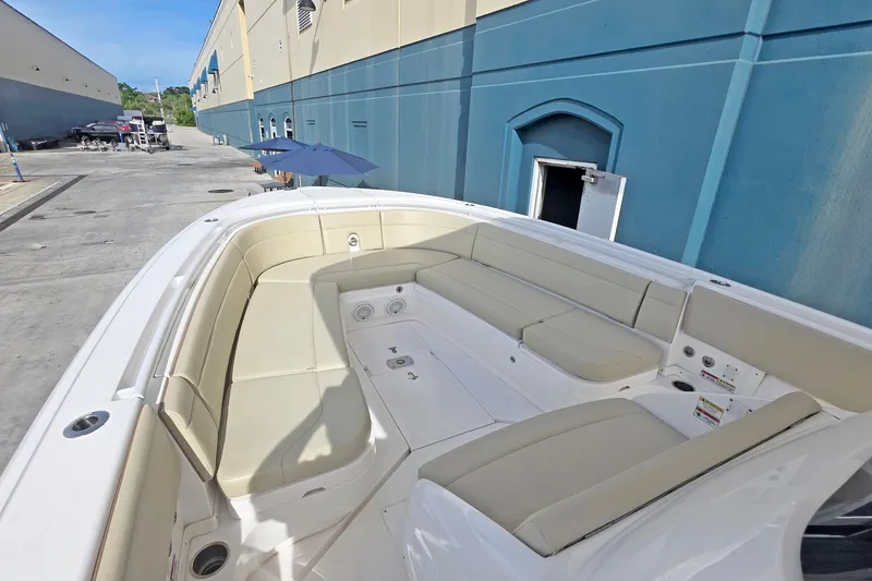 Slide: The Image of 2015 Intrepid 327 Center Console boat with beige seating, docked near a blue building. - 8