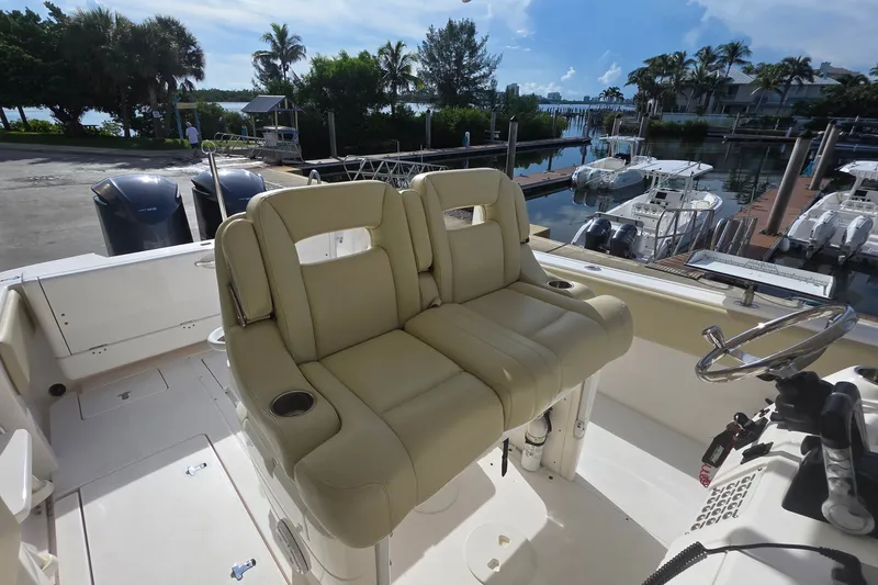 Slide: The Image of 2015 Intrepid 327 Center Console boat with beige seating, docked near a marina. - 18