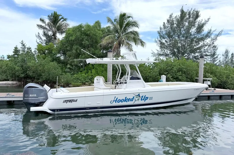 The Image of 2015 Intrepid 327 Center Console boat docked near lush greenery. - 10