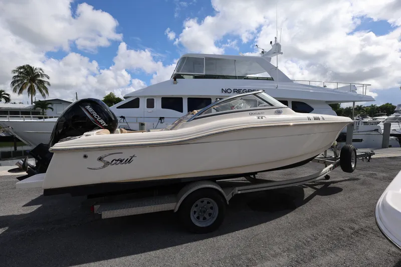 Slide: The Image of 2023 Scout 210 Dorado boat on trailer, parked near a marina under a cloudy sky. - 6