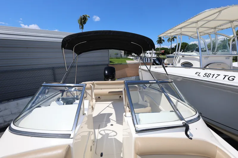 Slide: The Image of 2023 Scout 210 Dorado boat with canopy, docked beside another vessel, under clear blue sky. - 17