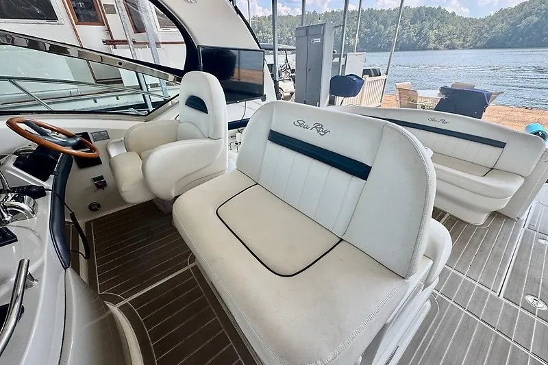 Slide: The Image of 2005 Sea Ray 390 Sundancer interior with white seating, wooden steering wheel, and lake view. - 24