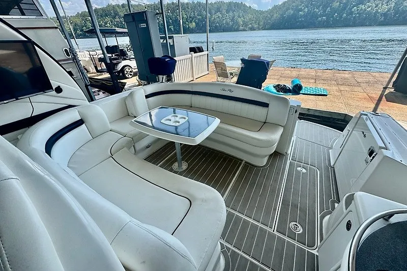 Slide: The Image of 2005 Sea Ray 390 Sundancer yacht interior with white seating and table, docked by a scenic lake. - 26