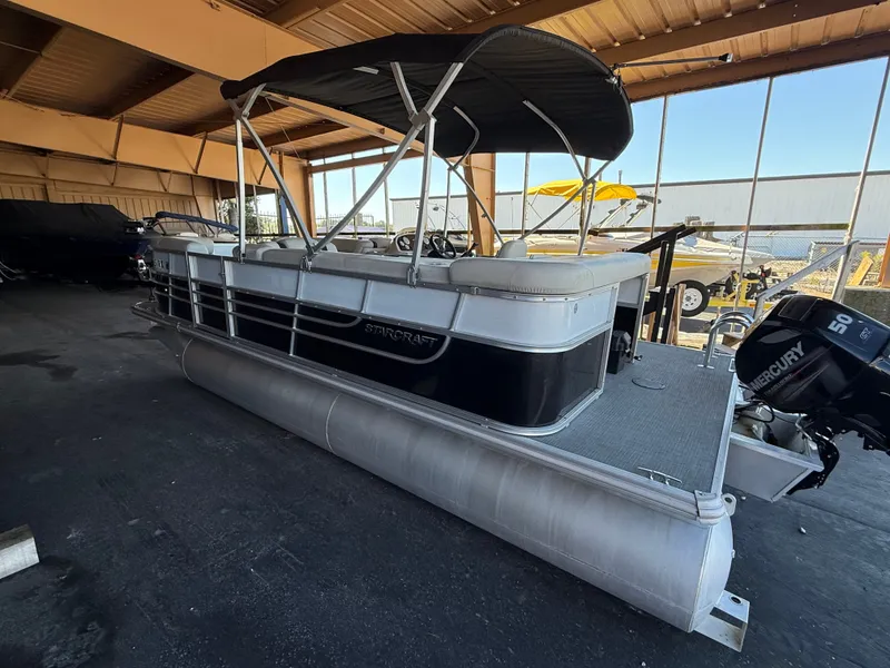 Slide: The Image of A 2017 Starcraft EX 20 C pontoon boat in a warehouse, featuring a black Bimini top. - 4