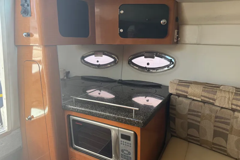 Slide: The Image of 2007 Chaparral 275 SSi boat interior with kitchenette, featuring stove, microwave, and seating area. - 14