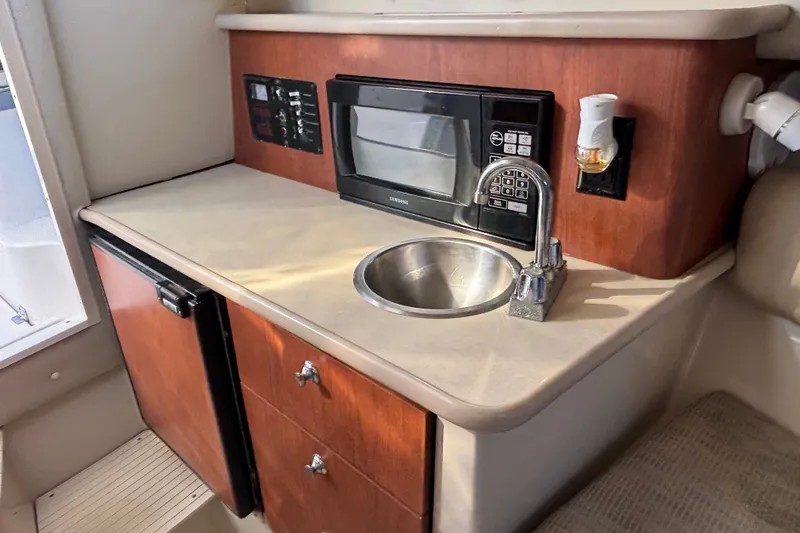 Slide: The Image of 2004 Robalo R245 Walkaround boat interior with kitchenette, featuring microwave, sink, and storage. - 15