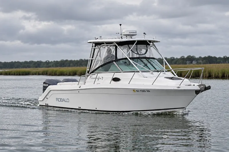Slide: The Image of 2004 Robalo R245 Walkaround boat cruising on a calm waterway under cloudy skies. - 0