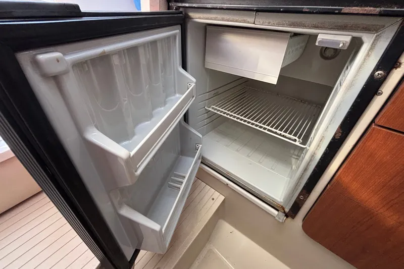 Slide: The Image of Open refrigerator inside 2004 Robalo R245 Walkaround boat, showing empty shelves and door compartments. - 17
