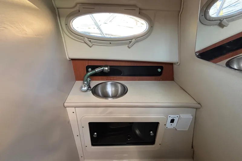 Slide: The Image of 2004 Robalo R245 Walkaround cabin sink area with oval window and storage compartment. - 21