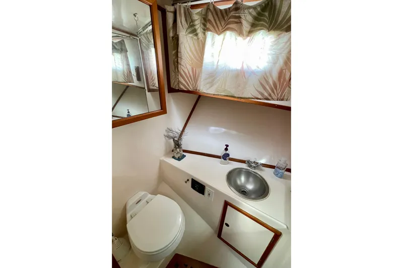 Slide: The Image of 1985 CHB 42 yacht bathroom with sink, toilet, mirror, and tropical curtains. - 50