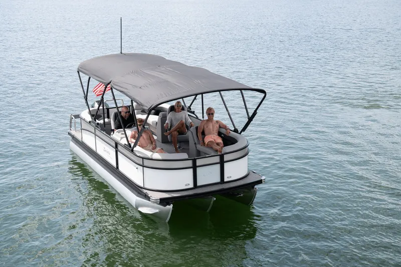 The Image of A 2026 Barletta Aria 22 QC pontoon boat on calm water. Four people relax under a black canopy. - 0