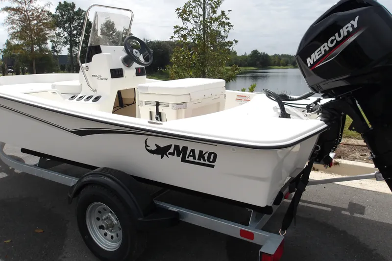 Slide: The Image of 2027 Mako Pro Skiff 15 CC boat with Mercury engine on trailer by a lake. - 2