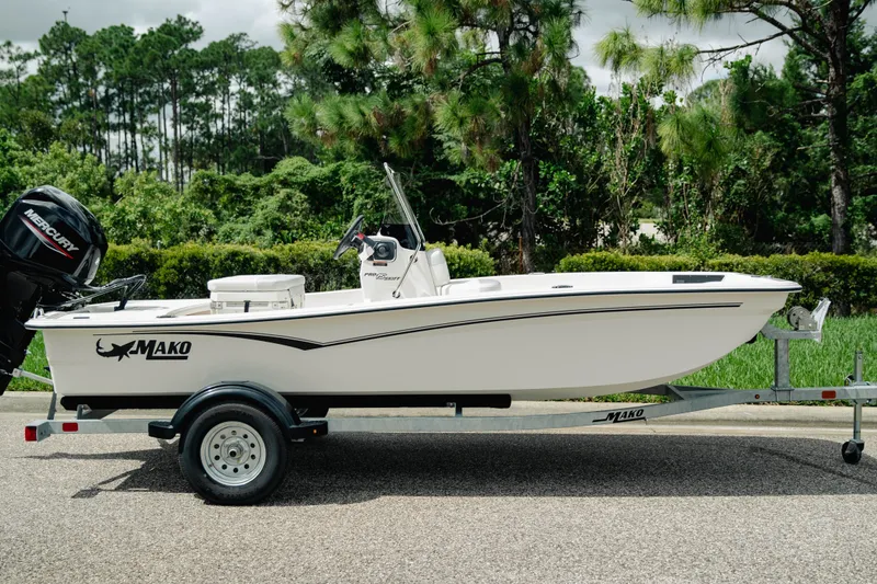 Slide: The Image of 2027 Mako Pro Skiff 15 CC boat on trailer, surrounded by lush greenery. - 1