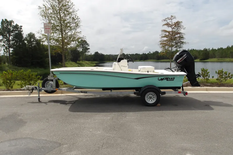 The Image of 2027 Mako Pro Skiff 15 CC boat on trailer by a scenic lake. - 1