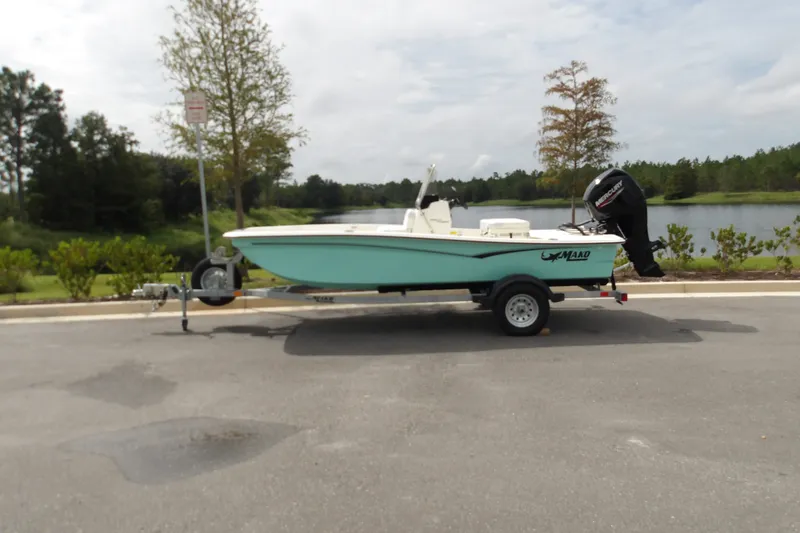 Slide: The Image of 2027 Mako Pro Skiff 15 CC boat on trailer by a scenic lake. - 2