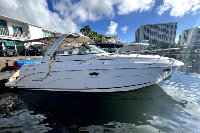 The Image of 2009 Rinker 300 Express Cruiser docked near waterfront buildings under a blue sky. - 0