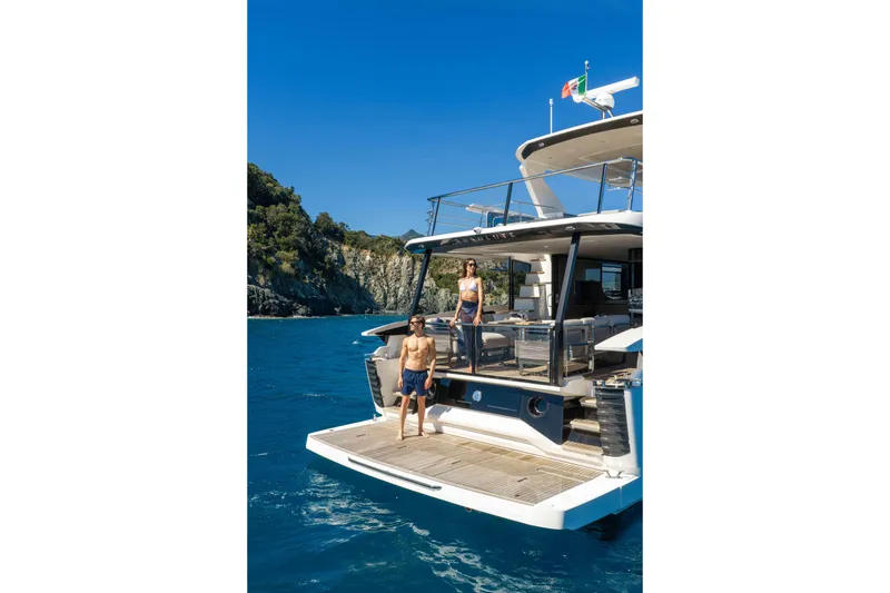 Slide: The Image of 2026 Absolute Navetta 58 yacht with people enjoying the sun, near rocky coastline. - 5