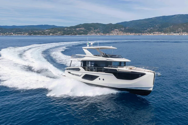 Slide: The Image of 2026 Absolute Navetta 58 yacht cruising on open sea with scenic coastal backdrop. - 2